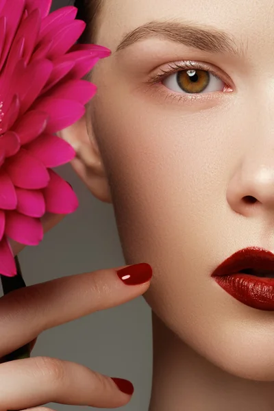 Close-up shot of sexy woman lips with red lipstick and beautiful pink flower. Perfect clean skin, fashion lip make-up. Beautiful spa portrait with tender pink  flower. Spa and cosmetics