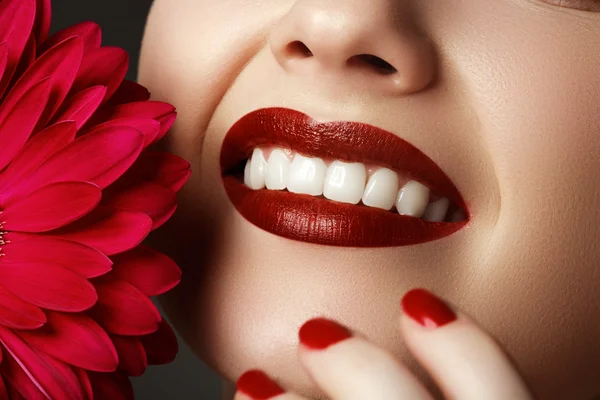 Close-up shot of sexy woman lips with red lipstick and beautiful pink flower. Perfect clean skin, fashion lip make-up. Beautiful spa portrait with tender pink  flower. Spa and cosmetics