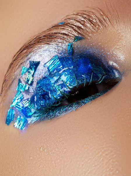 Cosmetics and make-up. Closeup macro shot of fashion sparcle visage. Closeup portrait of beautiful young woman with blue foil on face. Creative makeup