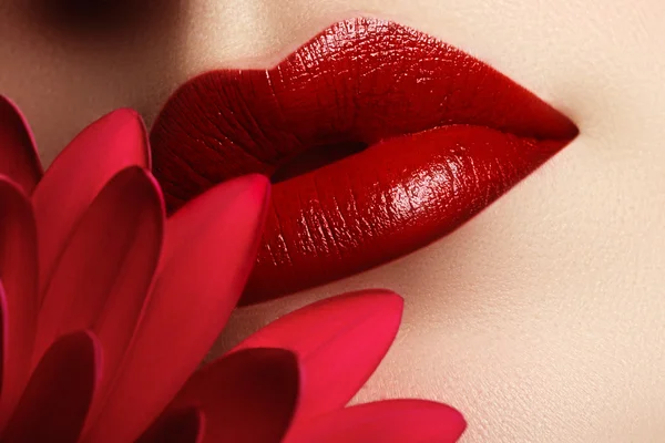 Close-up beautiful female lips with bright red makeup. Perfect clean skin, sexy lip make-up. Beautiful spa portrait with tender red  flower. Spa and cosmetics