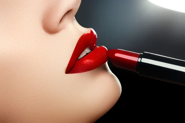 Beauty lips. Beautiful lips close-up, great idea for the advertising of cosmetics. Extreme close up on model applying red lipstick. Makeup. Professional fashion retro make-up. Red lipstick