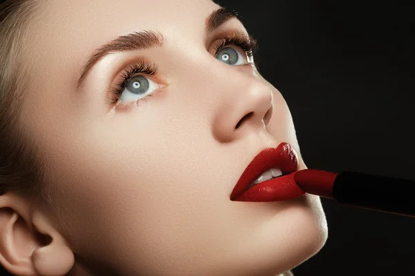 Beauty lips. Beautiful lips close-up, great idea for the advertising of cosmetics. Model applying red lipstick. Makeup. Professional fashion retro make-up. Red lipstick