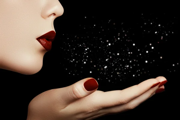 Beautiful young woman blowing a kiss from her hand. Model with perfect dark redl lips and manicured red nails