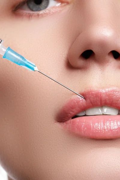 Closeup of beautiful woman gets injection in her lips. Full lips. Beautiful face and the syringe (plastic surgery and cosmetic injection concept). Botox injections.