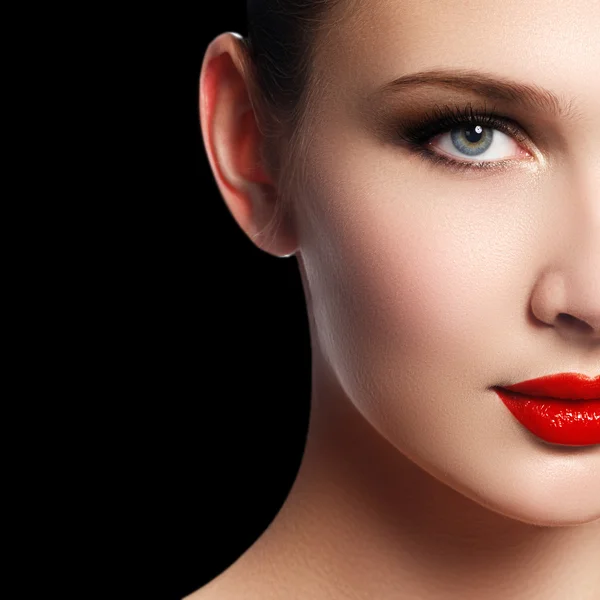 Make-up and cosmetics. Beauty woman face isolated on black background. Beautiful model girl makeup. Gorgeous lady with blue eyes and brown hair. Perfect skin. Professional make up. Red lips