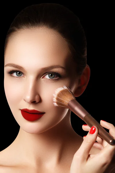 Make-up and cosmetics. Beauty woman face isolated on black background. Beautiful model girl makeup. Gorgeous lady with blue eyes and brown hair. Perfect skin. Professional make up. Red lips
