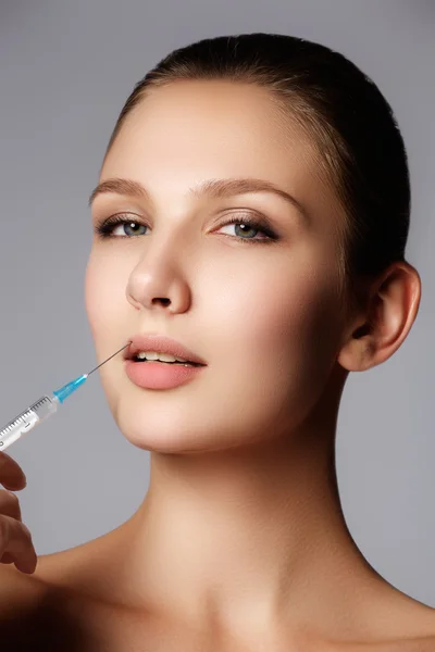 Closeup of beautiful woman gets injection in her lips. Full lips. Beautiful face and the syringe (plastic surgery and cosmetic injection concept).