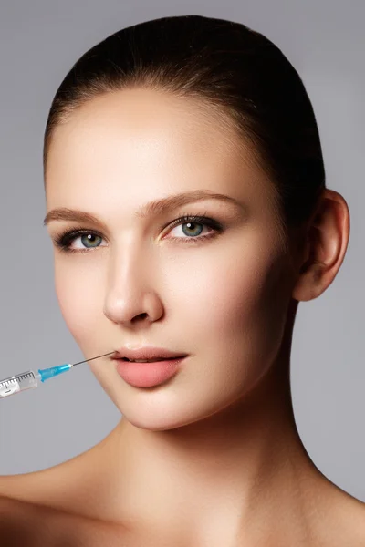 Closeup of beautiful woman gets injection in her lips. Full lips. Beautiful face and the syringe (plastic surgery and cosmetic injection concept)