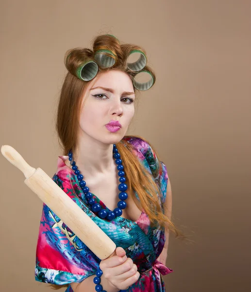 Woman housewife with a rolling pin in a bathrobe and curlers Fun