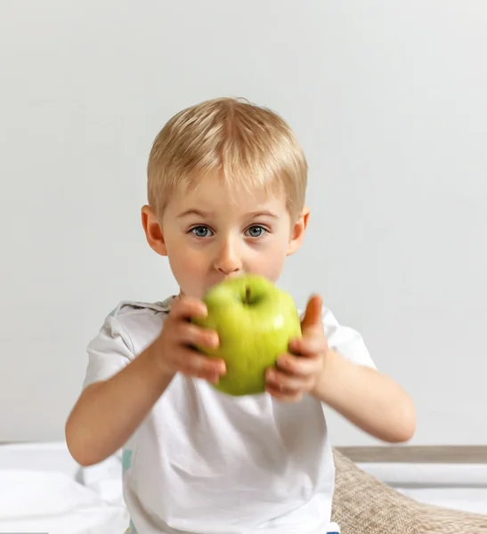 Happy cheerful boy eats the big apple, the child is the fruit gr