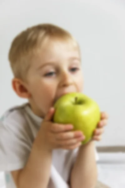 Happy cheerful boy eats the big apple, the child is the fruit gr