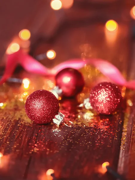 Red Christmas balls and golden glitter spilled on brown boards.