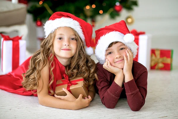 Children wearing Santa Claus sitting with gifts under the Christmas tree