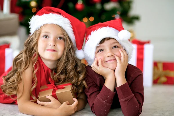 Children wearing Santa Claus sitting with gifts under the Christmas tree