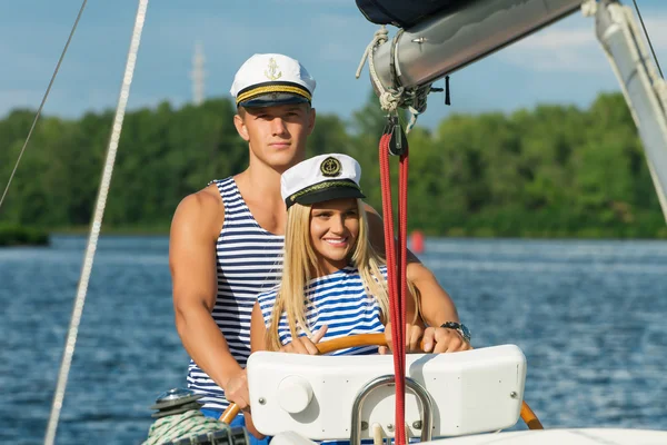 Young couple man and woman sailors at the helm of yacht.