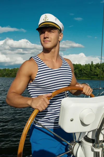 Young man sailor at the helm of yacht.
