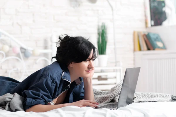 Lying on bed woman looking at laptop