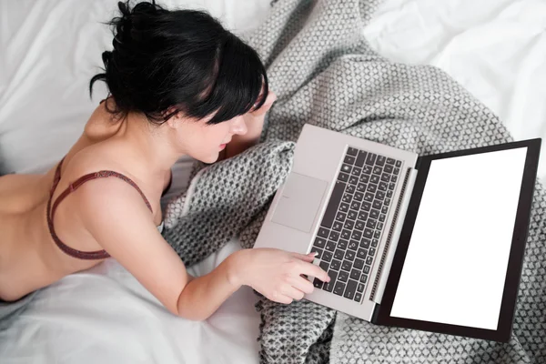 Naked woman using laptop with empty screen in bed