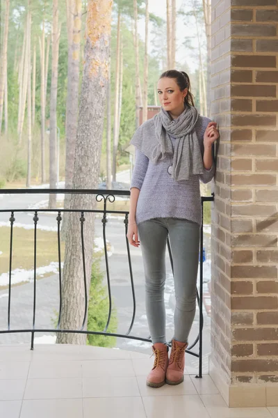 Attractive lady in sweater and scarf standing on balcony