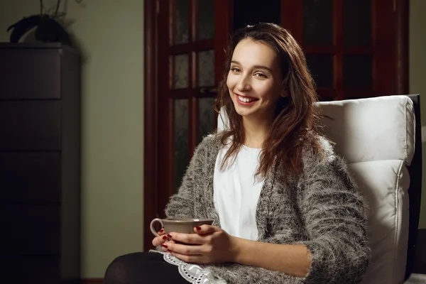 Happy smiling girl with big cup of tea in her hands on armchair