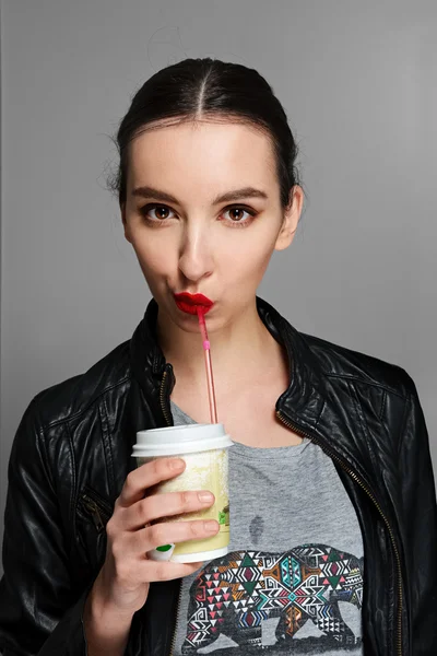 Young pretty girl in leather jacket drinks through straw from ca