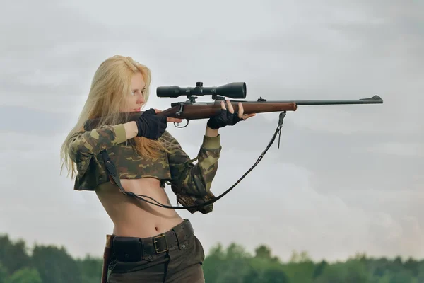 Pretty hunter girl aiming with hunting rifle in the outer wood.