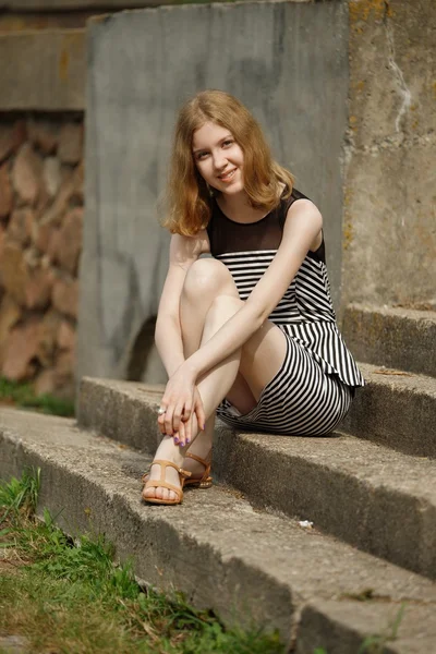 Pretty young teenage girl in striped dress sits on stairs
