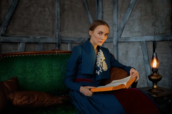 Attractive lady reading ancient book near vintage kerosene lamp