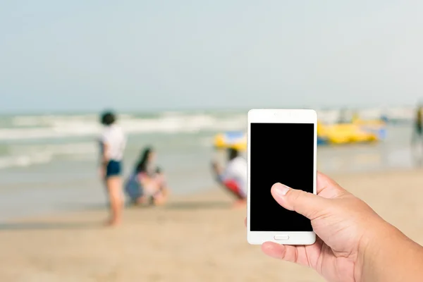 Man hand hold and touch screen smart phone on blurred beautiful people on the beach background.