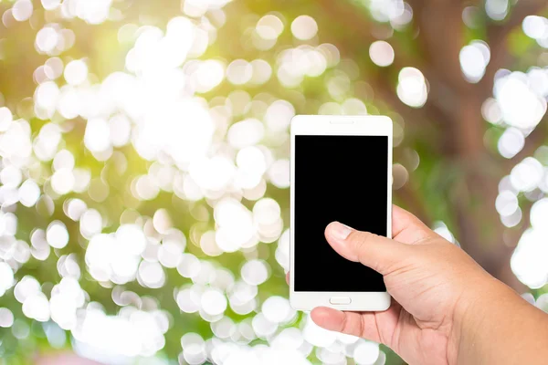 Man hand hold and touch screen smart phone on day noon light with green blurred nature background.