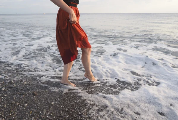 Girl in barefoot at the shore with red skirt