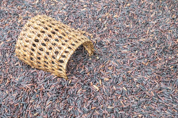 Closeup pile of black rice called riceberry rice with wooden wickerwork, rice with high nutrients on blurred riceberry textured background