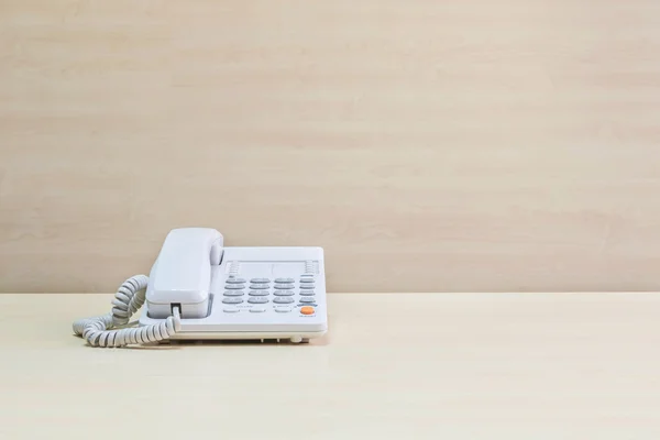 Closeup white phone , office phone on blurred wooden desk and wall textured background in the meeting room under window light