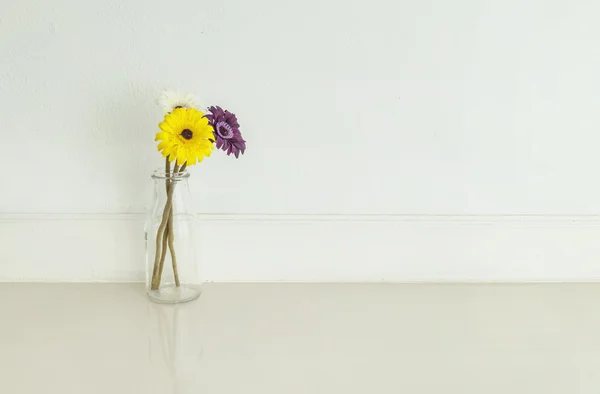 Closeup artificial colorful flower on transparent glass bottle on blurred marble floor and white cement wall textured background , fake white orchid flower