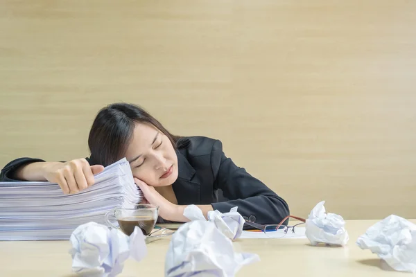 Closeup working woman sleeping after she tired from her work with work paper and document file on blurred wooden desk and wall textured background in the meeting room , tired working woman concept