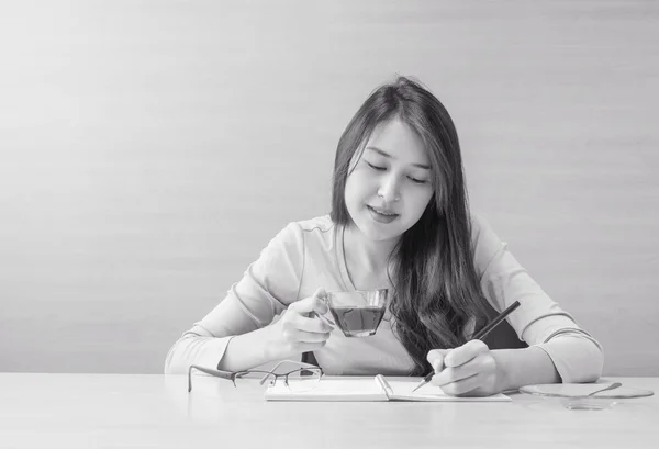 Working woman sit for drinking coffee in cup of coffee with thinking emotion in relax time on wood desk and wall textured background , coffee break of working woman concept in black and white tone