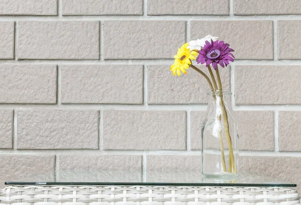 Closeup artificial colorful flower on transparent glass bottle on wood weave table on blurred brown brick wall texture background , beautiful interior in relaxation concept of house