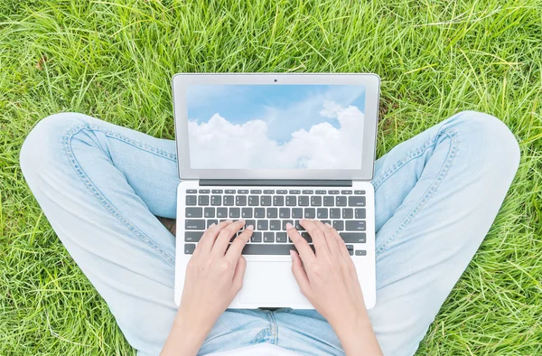 Asian woman sitting on grass floor in the garden textured background for use a notebook computer with blue sky in screen of notebook , work concept at the outdoor