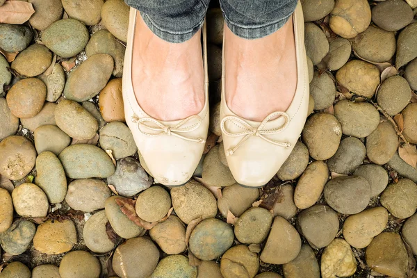 Vintage closeup woman foot with cream shoes on stones background