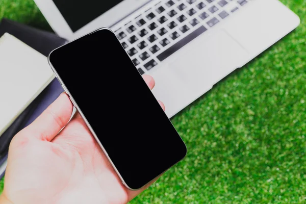 Blank notebook, phone, laptop and headphone on green grass