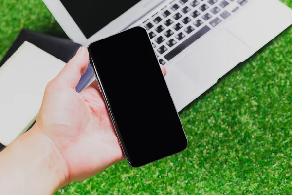 Blank notebook, phone, laptop and headphone on green grass