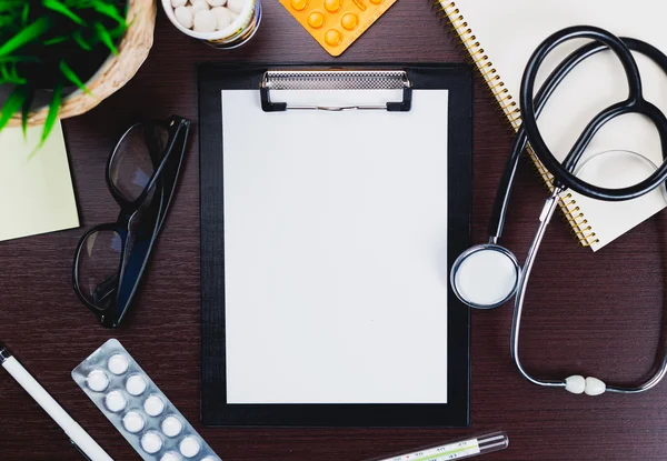 Medical clipboard and stethoscope on wooden desk background.