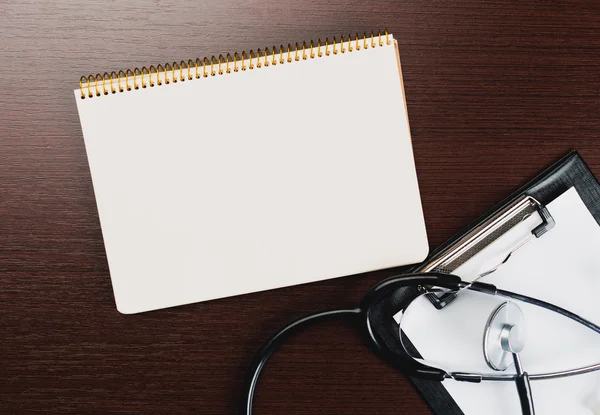 Medical clipboard and stethoscope on wooden desk background.