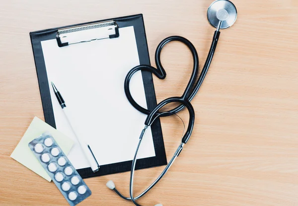 Medical clipboard and stethoscope on wooden desk background.