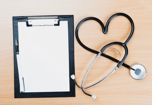 Medical clipboard and stethoscope on wooden desk background.