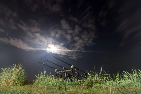 Carp spinning reel angling rods on pod standing. Night Fishing, Carp Rods, Cloudscape Full moon over lake.