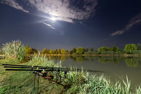 Carp spinning reel angling rods on pod standing. Night Fishing, Carp Rods, Cloudscape Full moon over lake.