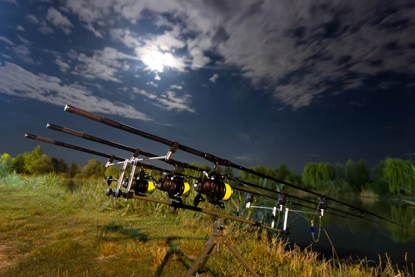 Carp spinning reel angling rods on pod standing. Night Fishing, Carp Rods, Cloudscape Full moon over lake.