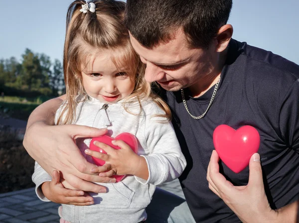 Man and baby holding a two red plastic heart. father hugs the daughter