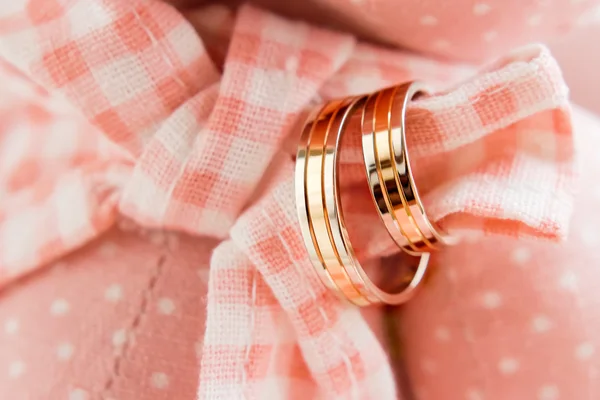 Golden wedding rings on pink plaid fabric. Wedding jewelry details.